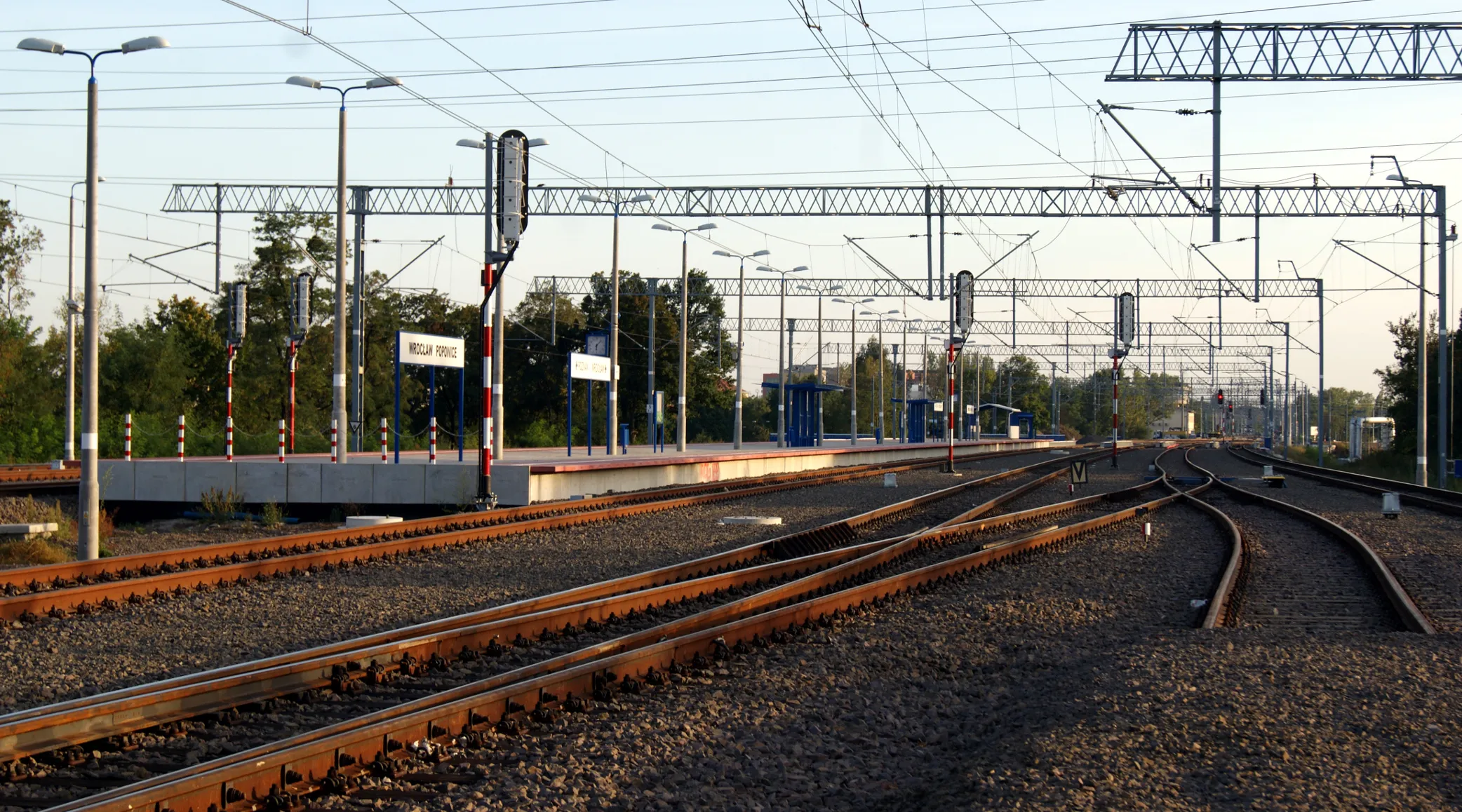 Tory i perony przystanku Wrocław Popowice pod siecią trakcyjną; tablica z nazwą stacji.