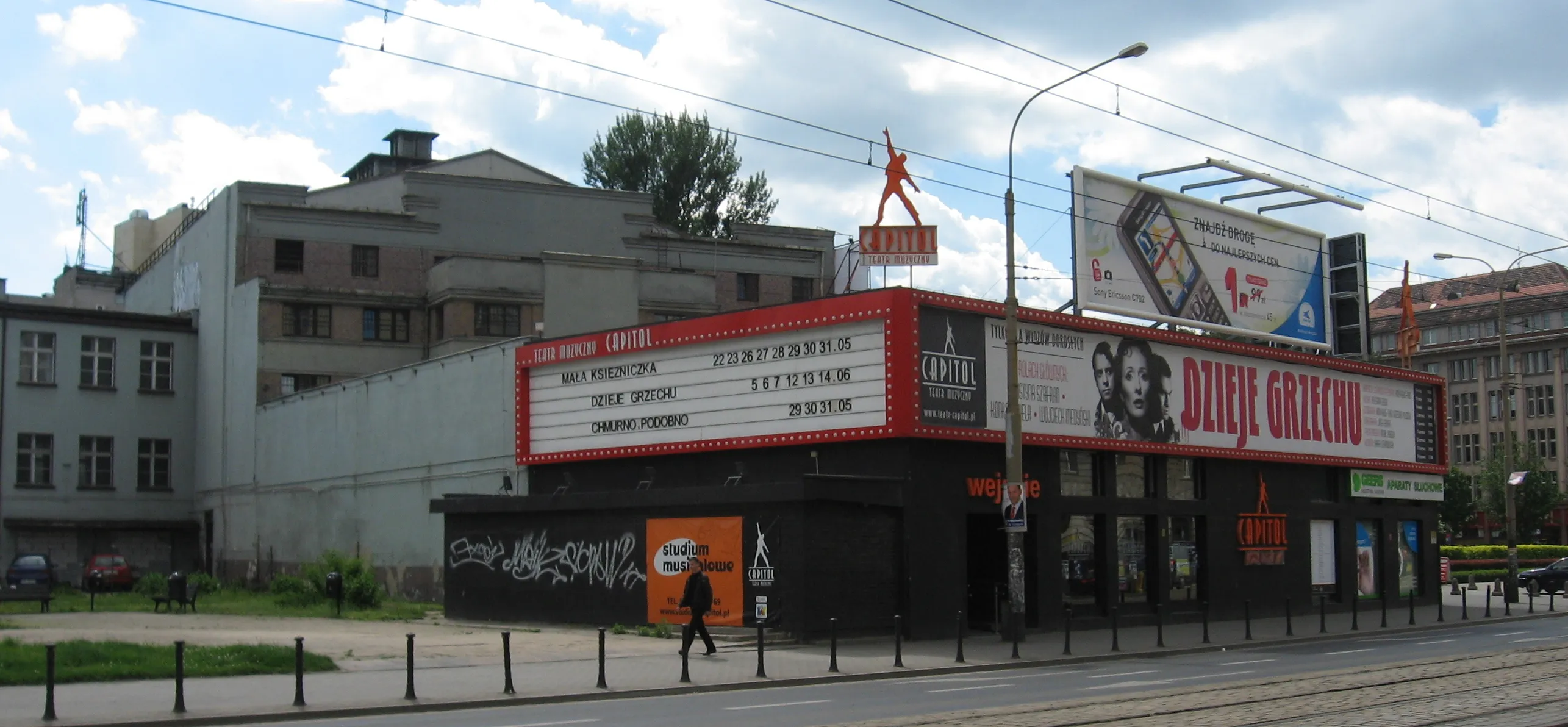 Niski front Teatru Muzycznego Capitol z czerwonym neonem, afiszami i graffiti; w głębi stara bryła teatru.