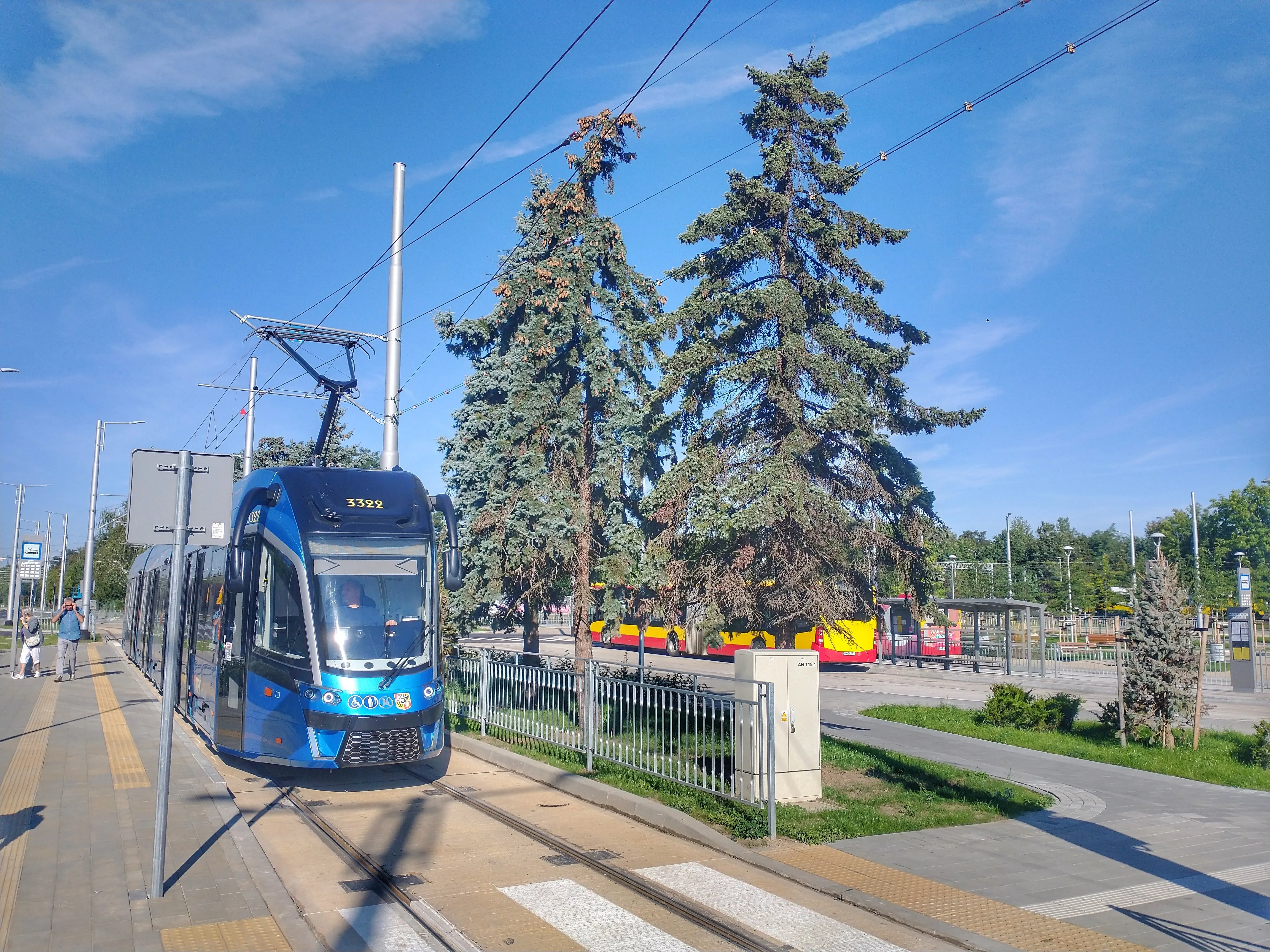 Niebieski tramwaj na nowej pętli Nowy Dwór, obok peronu z pasem ostrzegawczym i autobusów.
